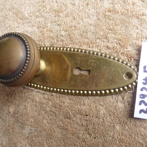 May include: Antique brass door knob and backplate. The round knob has a beaded edge and a tarnished finish. The backplate is oval with a keyhole and a beaded border. The tag reads "22924 E".