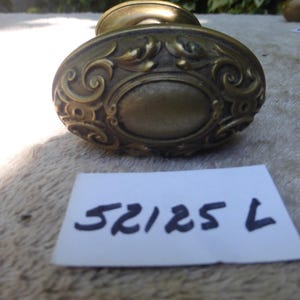 May include: Vintage brass door knob featuring an oval centre and elaborate scrollwork. The knob has a warm, aged brass hue. A white label with the number "52125 L" is in the foreground.