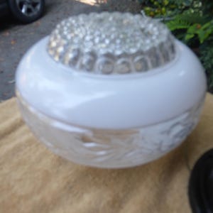 May include: A white and clear glass ceiling light fixture. The fixture has a round, frosted glass base with a floral design. The top is a white, rounded section with a clear, textured glass center.