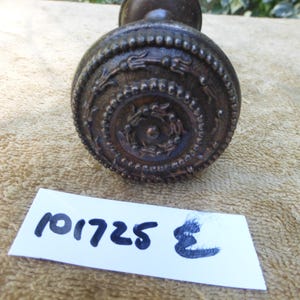 Könnte beinhalten: Ein dunkelbronze-farbener Türknauf mit aufwendigen geprägten Details. Der Knauf hat eine abgerundete Form mit einem dekorativen Muster aus Kreisen und floralen Designs. Die Nummer "101725" ist auf einem weißen Etikett aufgedruckt.