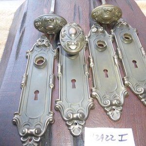 May include: Set of three antique brass door handles with ornate details. Each piece features a keyhole and a decorative knob. The backplates are rectangular with a scrolled design. The set is labelled "2922 I".