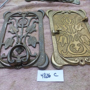 May include: Two antique metal decorative panels. One is open with a floral design and a handle. The other is a closed panel with a similar floral design. Both have a bronze finish and are rectangular.