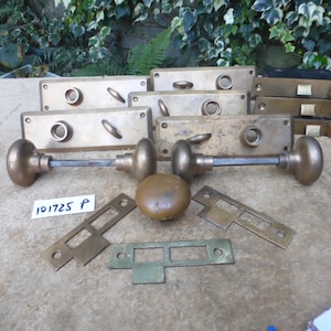 May include: Collection of antique brass door hardware, including doorknobs, lock plates, and latches. The hardware has a tarnished, aged appearance. The image includes a doorknob with a long rod and a separate round doorknob.