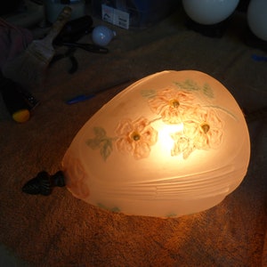 Może przedstawiać: Klosz lampy wykonany z matowego szkła z kwiatowym wzorem w odcieniach różowego i zielonego. Klosz jest podświetlony od wewnątrz, dając ciepłe światło.