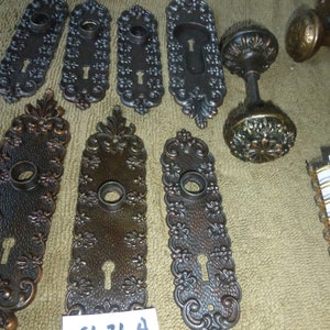 May include: A collection of antique door hardware, including ornate door plates and a decorative door knob. The door plates are made of metal and have a dark brown finish. The door knob is also made of metal and has a similar finish. The door plates have intricate designs and the door knob has a floral design. The door hardware is in good condition and would be a great addition to any home.