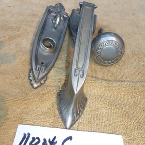 May include: A set of three antique door hardware pieces in a silver finish. The set includes a door handle, a door knob, and a door plate. The door handle has a decorative design with a geometric pattern. The door knob has a simple design with a circular shape. The door plate has a rectangular shape with a keyhole and a decorative design. The set is labeled "11224 C".