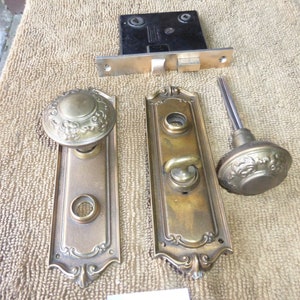 May include: Set of antique brass door hardware, including a door knob, a door handle, and a door latch. The hardware has an ornate design with floral motifs.