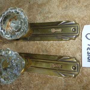 May include: Pair of antique brass door knobs with clear glass crystal knobs. The knobs have a decorative art deco design.
