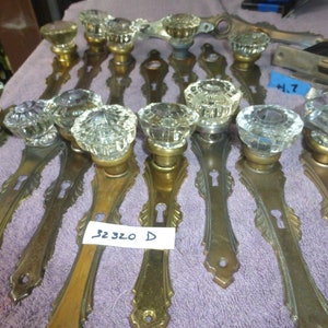 May include: A set of 10 antique brass door knobs with clear glass crystal knobs. The knobs have a decorative design and a keyhole. The knobs are labelled "32 320 D".
