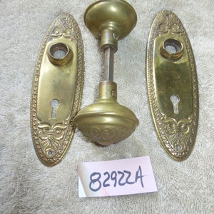 May include: A set of three antique brass door knobs with ornate designs. The knobs are oval shaped and have a keyhole in the centre. The set includes two backplates and one knob with a spindle.