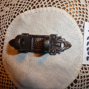 May include: A black cast iron wall hook with an ornate design. The hook is mounted on a white crocheted surface with a white tag that says "2023 M".