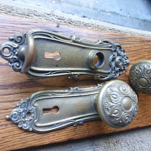 May include: Two ornate brass door knobs with keyholes and decorative details. The knobs are on a wooden surface with a white tag that says "42322 B".