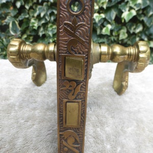 May include: Antique brass door hardware with a decorative, ornate design. The door handle has a keyhole and a latch. The door handle is attached to a decorative plate with a floral design.