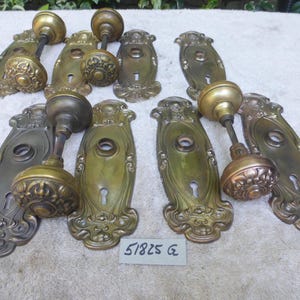 Puede incluir: Un surtido de herrajes de puertas antiguos, que incluyen varios pomos de latón y placas traseras ornamentadas. Los pomos tienen forma redondeada con detalles decorativos. Las placas traseras son alargadas con intrincados diseños florales. Los herrajes son de varios tonos de latón y bronce.