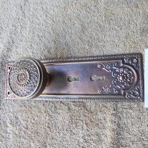 May include: Antique brass door hardware with a decorative floral design and a round knob. The hardware has a keyhole and is labeled "112322 K".