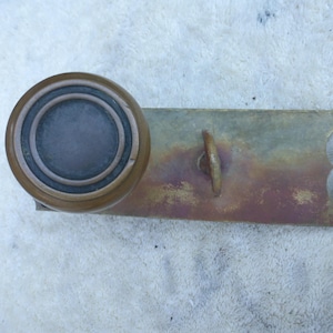 May include: An antique brass door handle with a circular knob and a rectangular backplate. The backplate features a small handle and decorative scrollwork. The brass has a weathered, aged appearance.