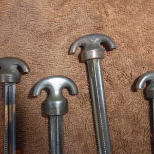 May include: Four metal tools with a three-pronged head. The tools are silver in color and have a threaded shaft.