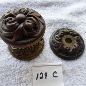 Puede incluir: Un par de pomos de puerta de bronce adornados con un diseño floral. Los pomos tienen la forma de un disco redondo con un centro elevado. Los pomos están sobre un fondo blanco.