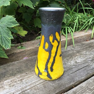 Peut inclure: Un vase en céramique jaune et noir avec un glaçage coulant. Le vase est haut et étroit avec une base arrondie.