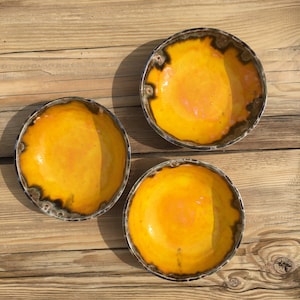 May include: Three yellow ceramic bowls with a dark brown rim. The bowls are on a wooden surface.