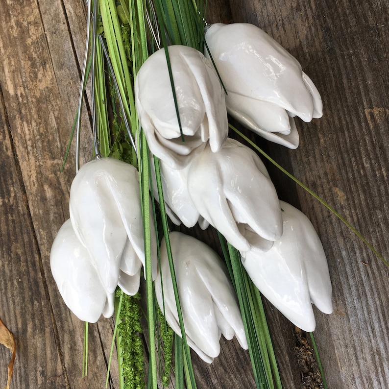 A bouquet of 9 handmade white ceramic tulips with green stems and leaves, laying on their sides on a wooden bench.