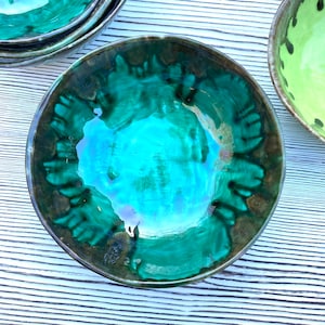 Può includere: Una ciotola in ceramica verde con una glassa screziata. La ciotola ha una forma rotonda e profonda e una finitura liscia e lucida.