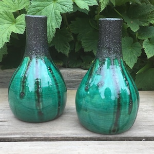 Op de afbeelding: Twee kleine groene keramische vazen met zwarte accenten. De vazen hebben een glanzende afwerking en een gestreept ontwerp.