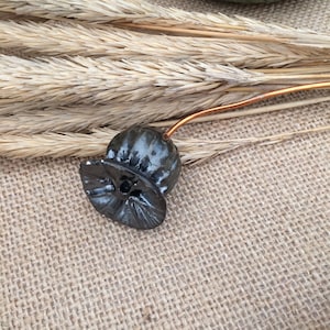 May include: A black ceramic poppy with a copper wire stem. The poppy is sitting on a burlap surface.