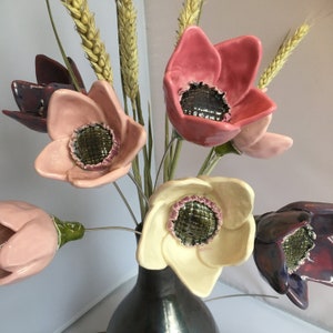 Pode incluir: Um buquê de flores de cerâmica em um vaso. As flores são rosa, brancas e roxas com centros pretos. O vaso é preto.
