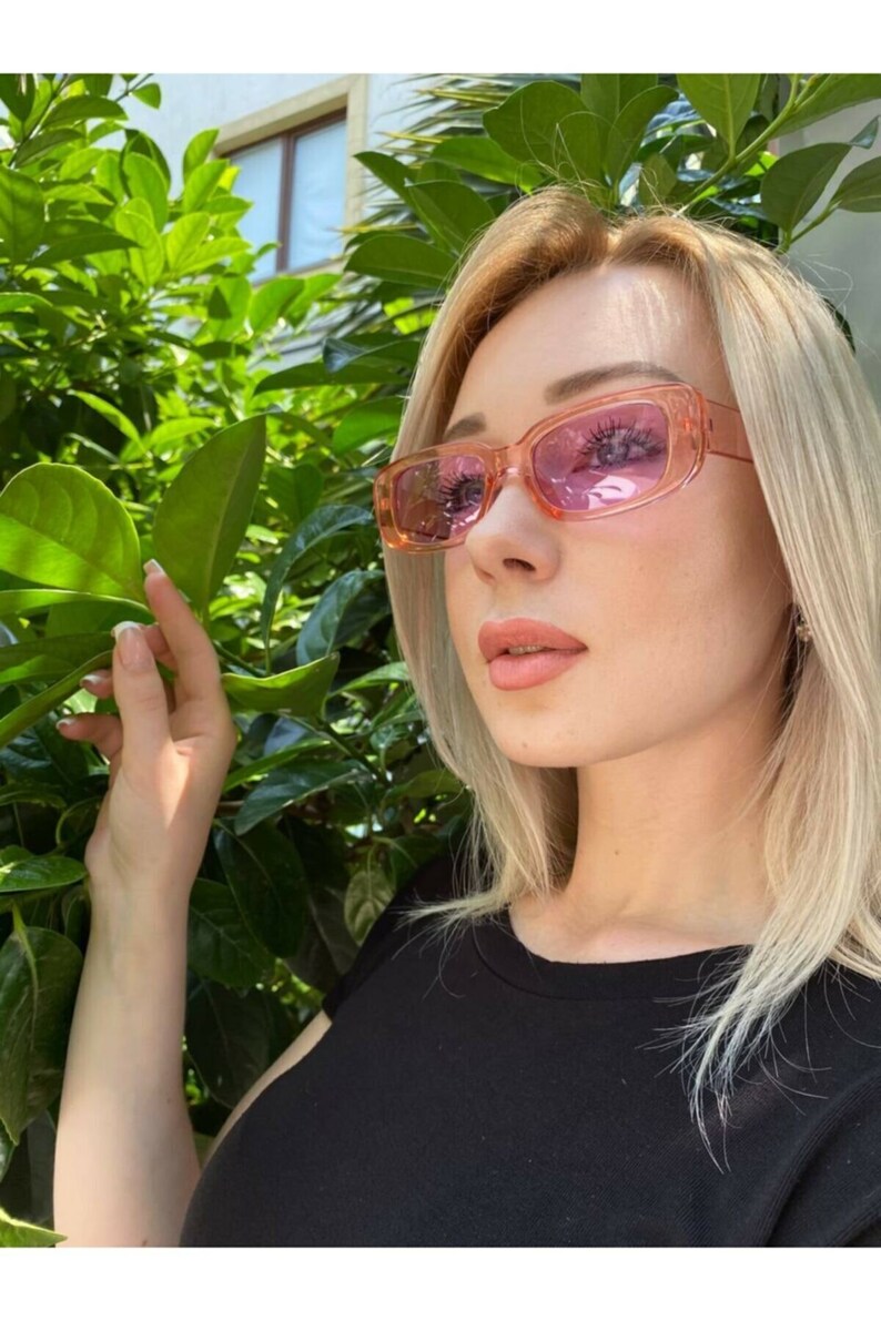 May include: A woman wearing pink rectangular sunglasses with a black t-shirt.
