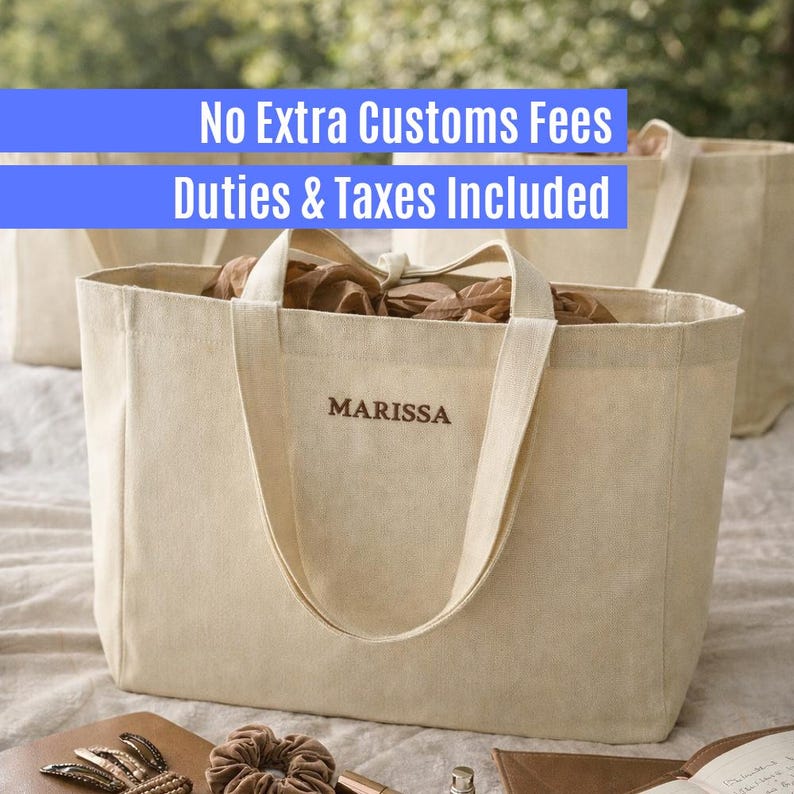 May include: A cream-colored canvas tote bag with two sturdy handles and the name MARISSA embroidered in brown thread on the front. The bag has an open top, revealing brown paper filler inside, and is constructed from a durable woven fabric.