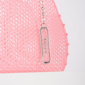 Pu&ograve; includere: Borsa tote in rete rosa con una catena argentata e un portachiavi in acrilico trasparente con la scritta "Jessica" stampata.