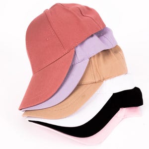 May include: A stack of six baseball caps in various colors, including pink, black, white, beige, lavender, and red.
