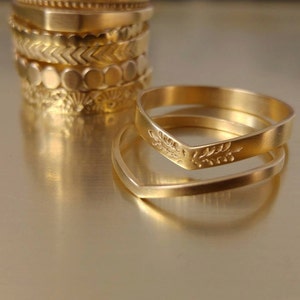 May include: Two gold rings, one with a V-shaped design and the other with a floral pattern, are stacked on top of each other.