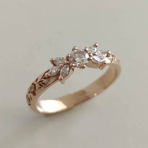 May include: A delicate rose gold ring with a floral design featuring a round centre diamond and smaller diamonds set in a leaf pattern.