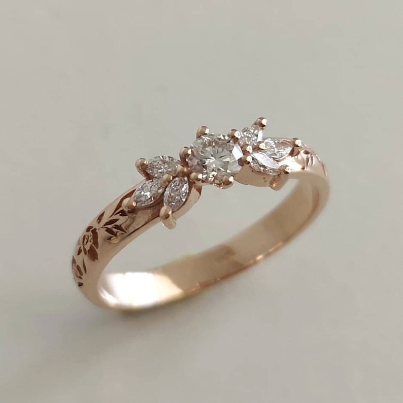 May include: A delicate rose gold ring with a floral design featuring a round centre diamond and smaller diamonds set in a leaf pattern.