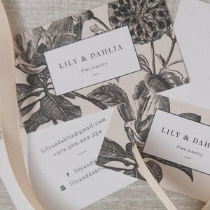 May include: Two business cards with a floral design. The text on the cards reads "Lily & Dahlia Fine Jewelry" and includes contact information.