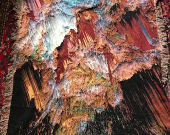 May include: Woven throw blanket with a colorful abstract design. The blanket features a mix of colors including red, orange, black, and blue. The edges are finished with a white fringe. The blanket is rectangular in shape.