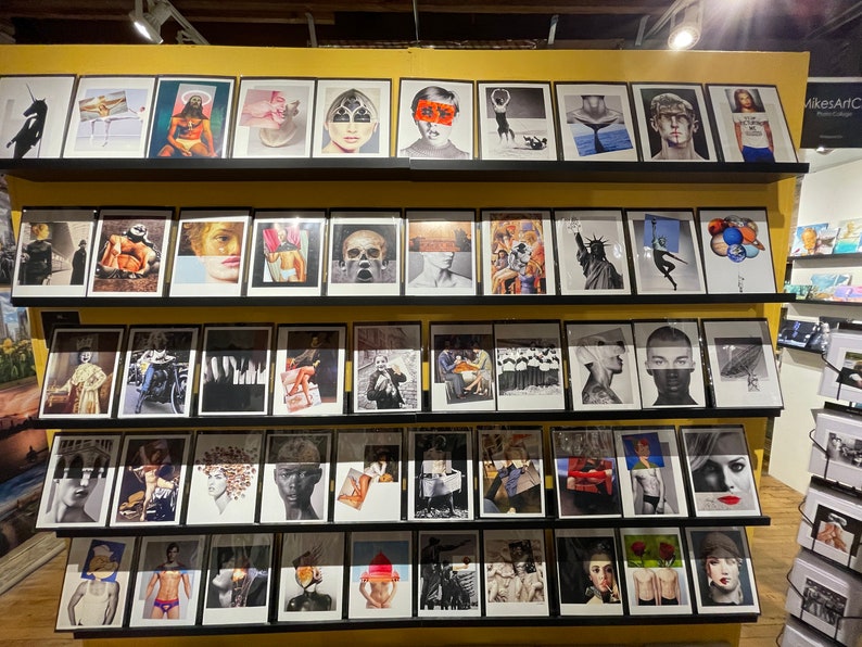 May include: A display of framed art prints featuring a variety of artistic styles and subjects. The prints are arranged on shelves, showcasing portraits, abstract designs, and surreal imagery. The color palette includes black, white, and pops of color, creating a visually diverse collection.