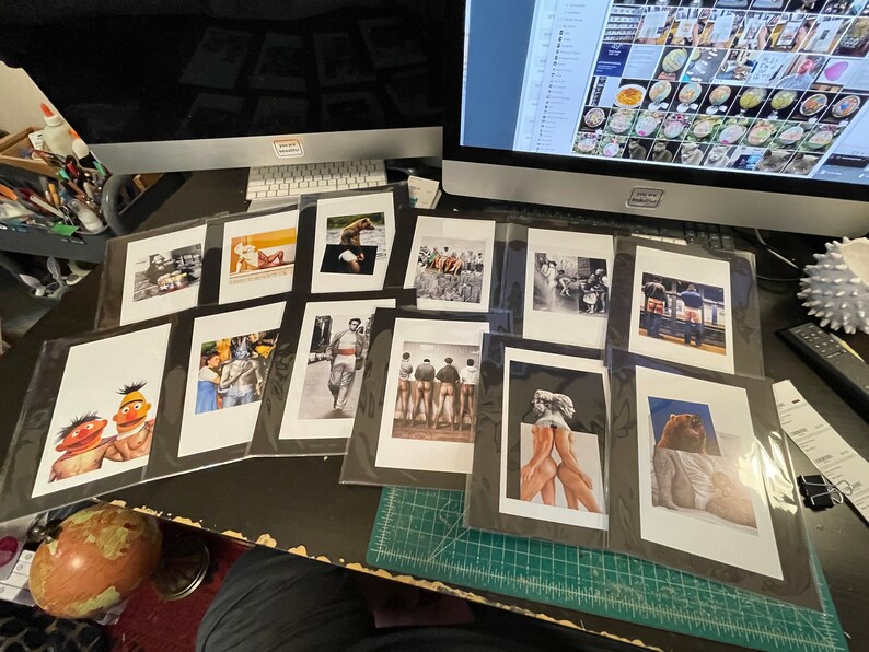 May include: A collection of framed art prints, displayed on a desk. The prints feature various images, including portraits, illustrations, and photographs. The artwork is diverse in style and subject matter, with some prints in black and white and others in color.