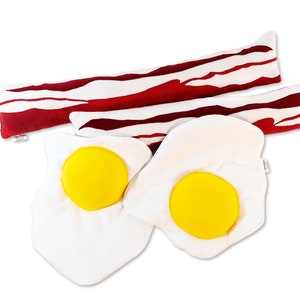 May include: Two white plush pillows shaped like fried eggs with yellow yolks, and two red and white striped plush pillows shaped like bacon.