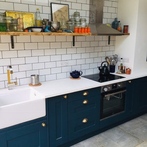 May include: A kitchen with white subway tile backsplash, dark blue cabinets, and a white countertop. The kitchen features a farmhouse sink, a stainless steel oven, and a black electric stovetop.
