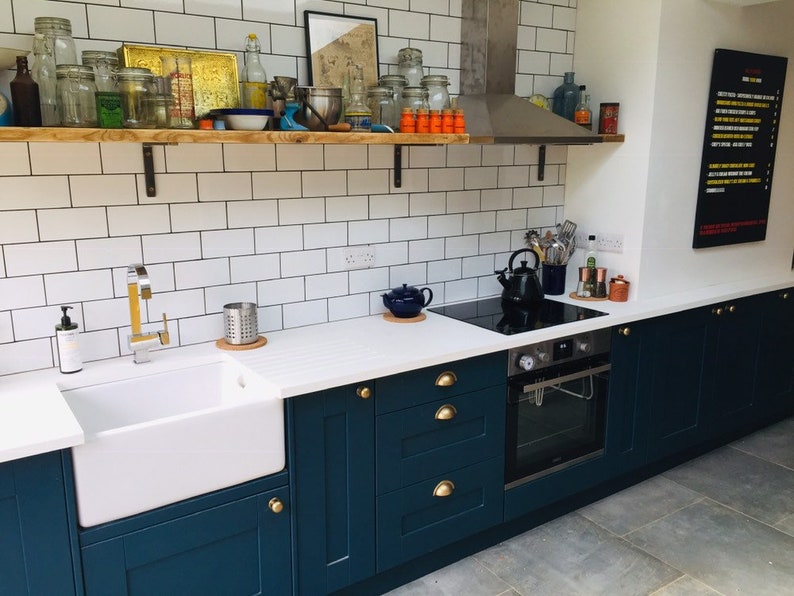 May include: A kitchen with white subway tile backsplash, dark blue cabinets, and a white countertop. The kitchen features a farmhouse sink, a stainless steel oven, and a black electric stovetop.