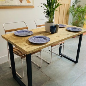 May include: A rustic wooden dining table with black metal legs and four white metal chairs. The table has a distressed wood finish and is decorated with blue and white patterned plates.