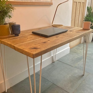 May include: A rustic wooden desk with a natural wood finish and white hairpin legs. A laptop computer, a potted plant, and a glass are on the desk.