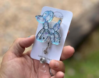 May include: A blue balloon dog badge reel with glitter accents. The badge reel is attached to a white card with the text "Southern Tutor Design Co." and a silver retractable clip.