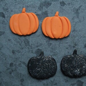 Puede incluir: Cuatro decoraciones de calabaza con tem&aacute;tica de Halloween. Dos son naranjas y dos son negras con purpurina.