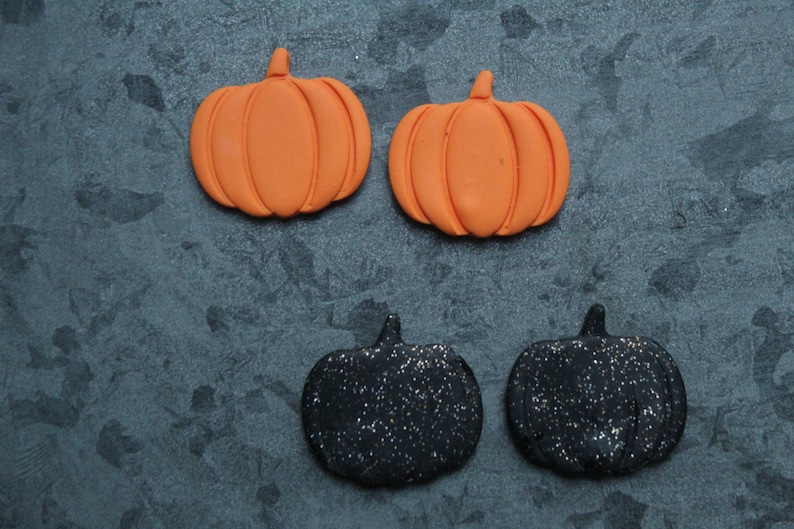 Puede incluir: Cuatro decoraciones de calabaza con tem&aacute;tica de Halloween. Dos son naranjas y dos son negras con purpurina.