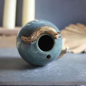 May include: A teal ceramic incense holder with a brown and tan slug design. The incense holder has a large opening and a small hole. The ceramic piece is on a gray surface.