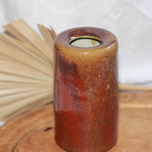 May include: A cylindrical ceramic vase with a wide opening. The vase has a gradient of colors, transitioning from a reddish-brown at the base to a lighter tan at the top. The surface has a glossy finish.